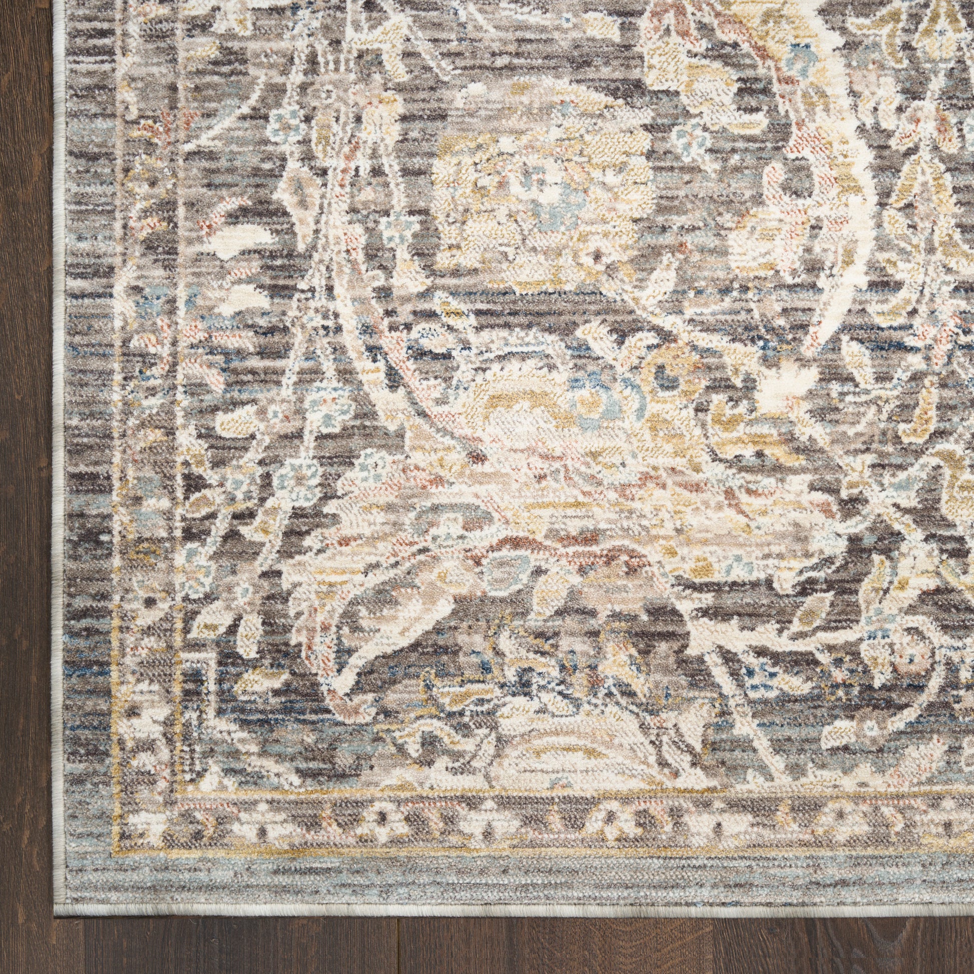 Grey-blue Persian-style ornate area rug corner with cream and gold floral motif on dark wood floor.