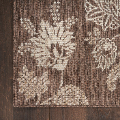 Brown floral woven rug with cream-beige flowers against a dark brown background; textured textile on wood floor.