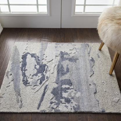 Cream rectangular rug with abstract blue-gray pattern on dark wood floor, beside glass doors; beige fur-stool with gold legs.