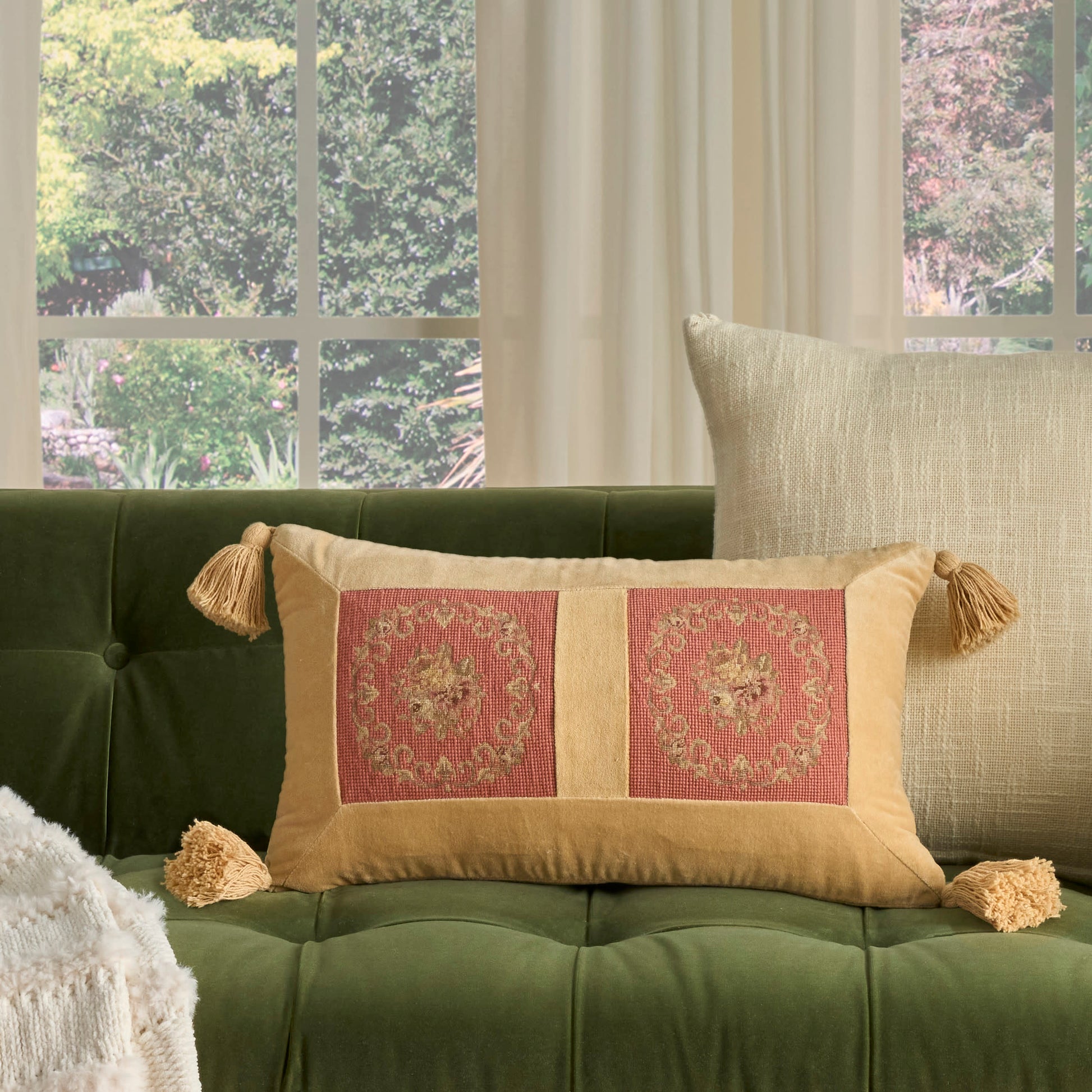 Olive tufted sofa with beige tasseled rectangle pillow featuring two pink medallion panels.