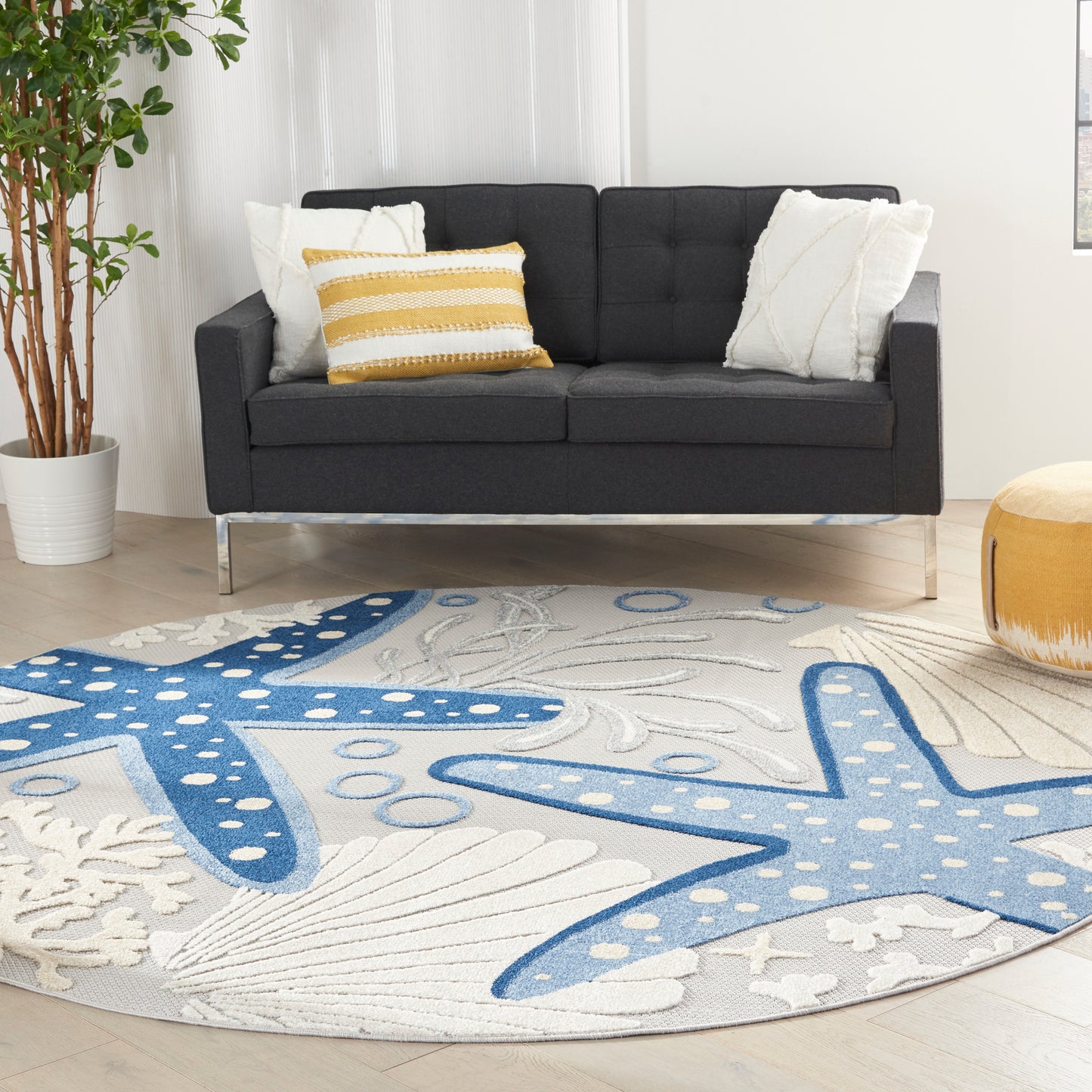 Round rug with blue starfish motifs on white background, plush fabric; pairs with a dark gray sofa.