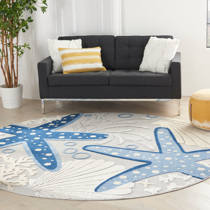 Round rug with blue starfish motifs on white background, plush fabric; pairs with a dark gray sofa.