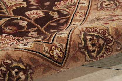 Close-up of an ornate oriental rug with brown, tan, cream and burgundy floral pattern, folded on a wooden floor.