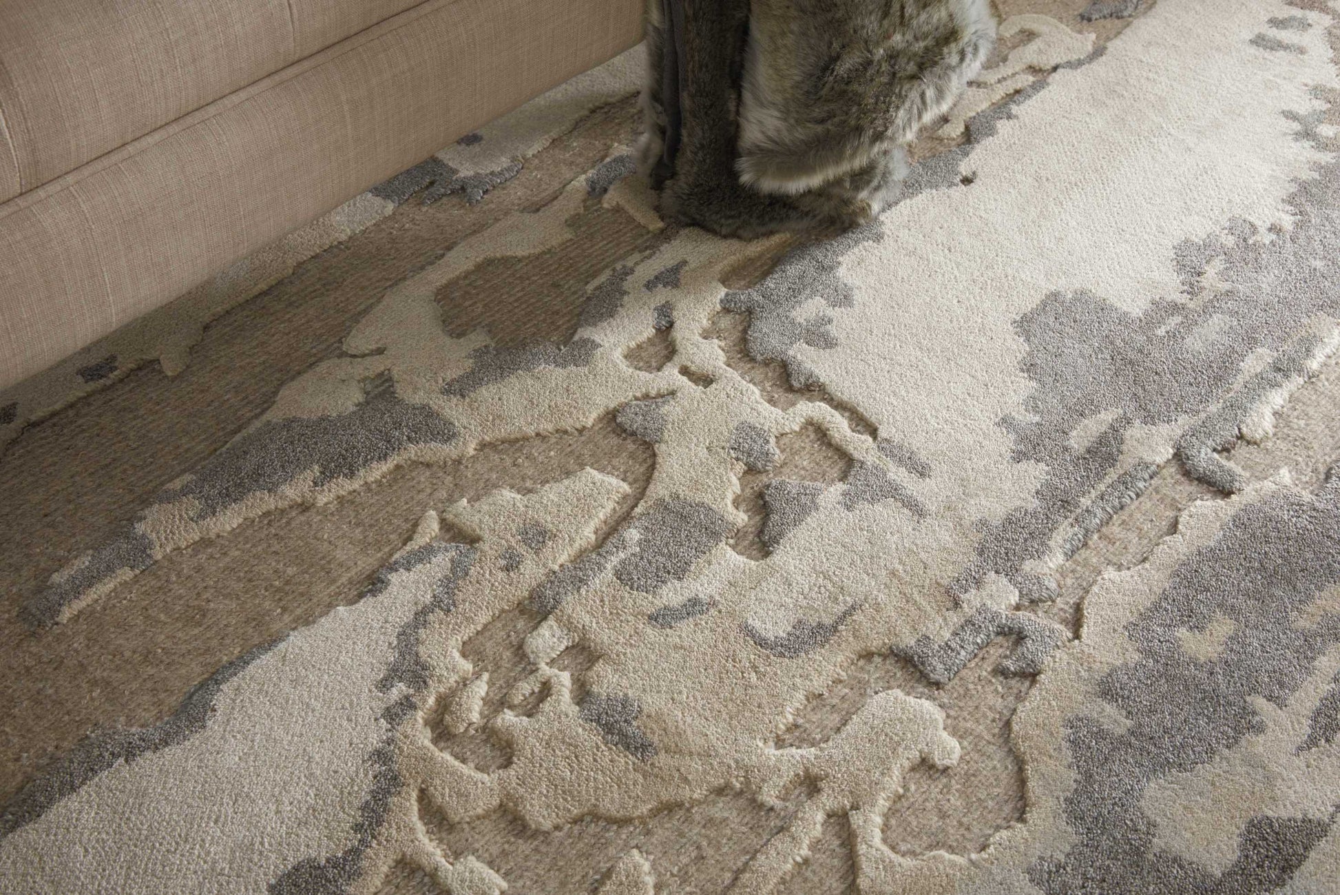 Neutral abstract-pattern rug in cream, beige and gray with a textured, raised pattern under a beige sofa.