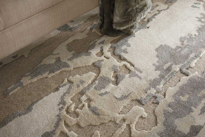 Neutral abstract-pattern rug in cream, beige and gray with a textured, raised pattern under a beige sofa.