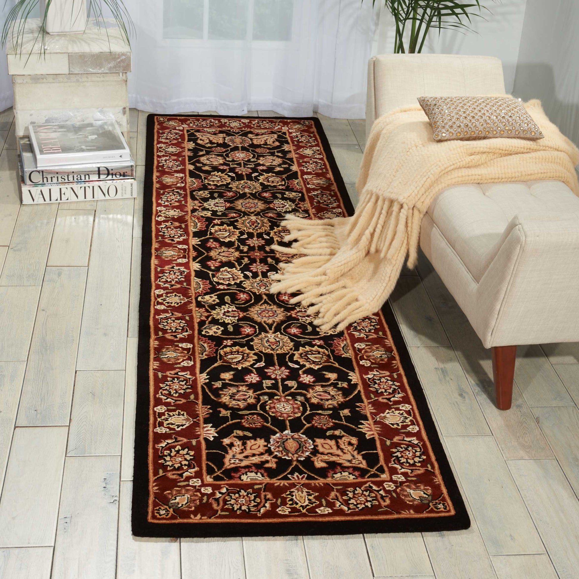 Round floral rug, 4 ft diameter, with a black center and red border, fringed edges, on a light wood floor beside a beige sofa with a throw.
