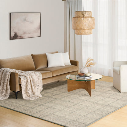 Neutral grid rug in a living room, with a tan leather sofa, white cushions, beige throw, round glass coffee table and a woven pendant light.