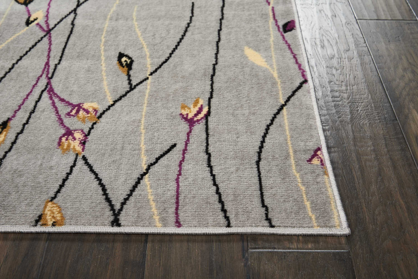 Grey abstract floral area rug with black, purple and yellow curved lines, light border, on dark wood floor.