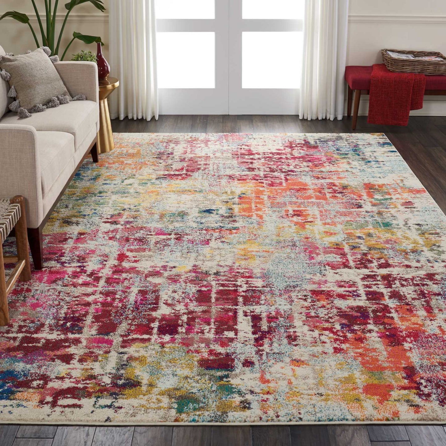 Multicolor abstract area rug in a modern living room with beige sofa, white curtains, and a red throw.