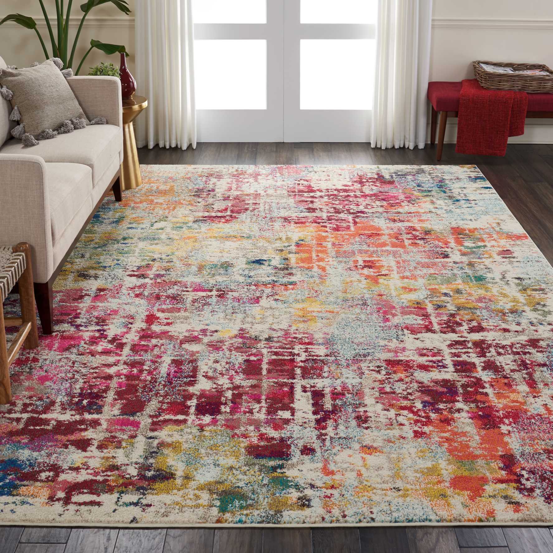 Multicolor abstract area rug in a modern living room with beige sofa, white curtains, and a red throw.