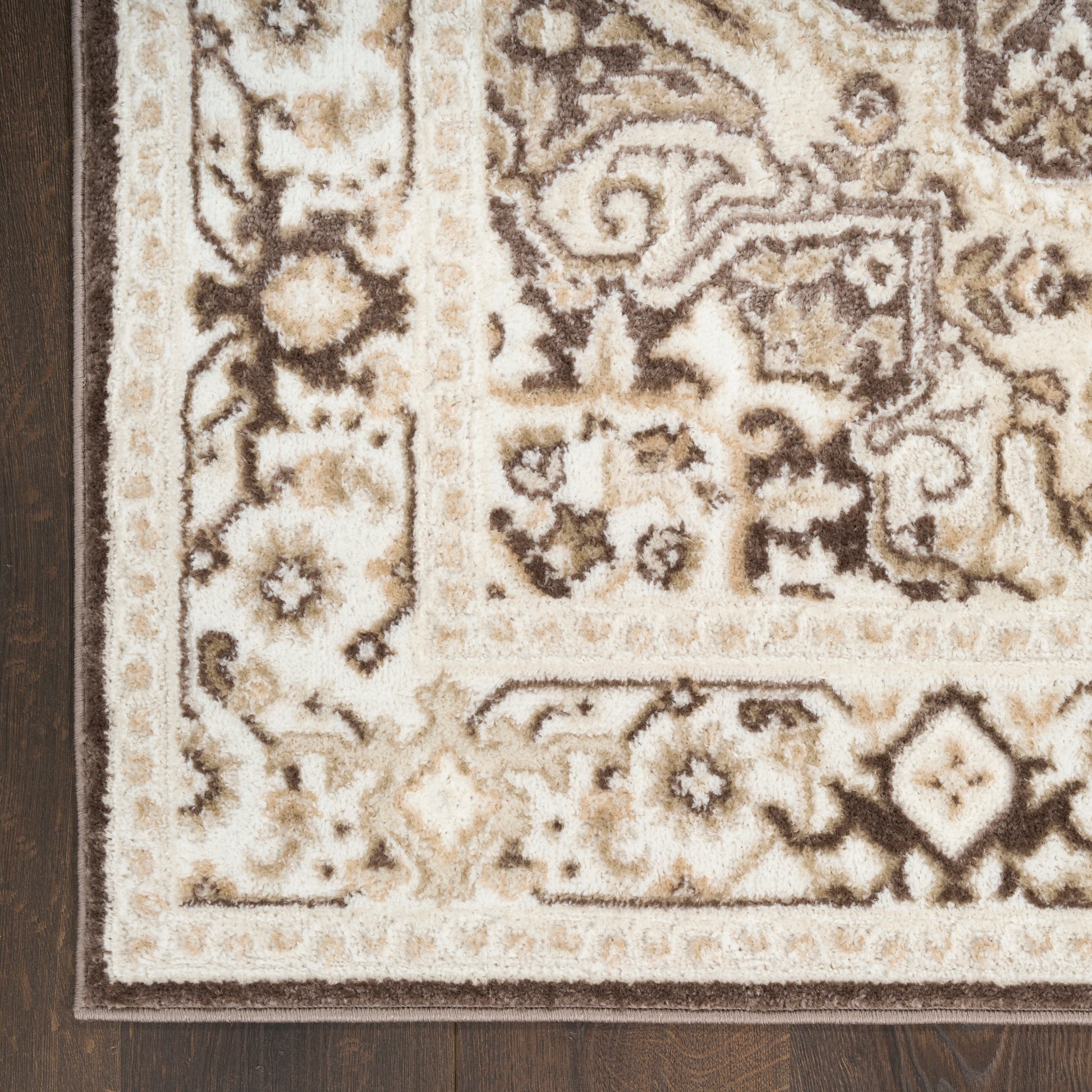 Beige cream ornate area rug & brown floral pattern with dotted border on dark wood floor.