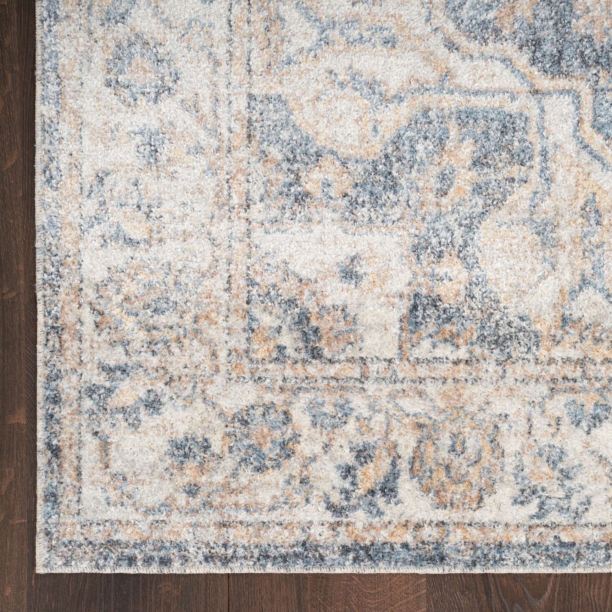 Blue, beige, and cream patterned area rug with floral motifs on dark wood floor; textured pile and light border.