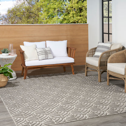Outdoor patio with white-cushioned wooden sofa, beige wicker chairs, and a gray textured leaf-pattern rug.