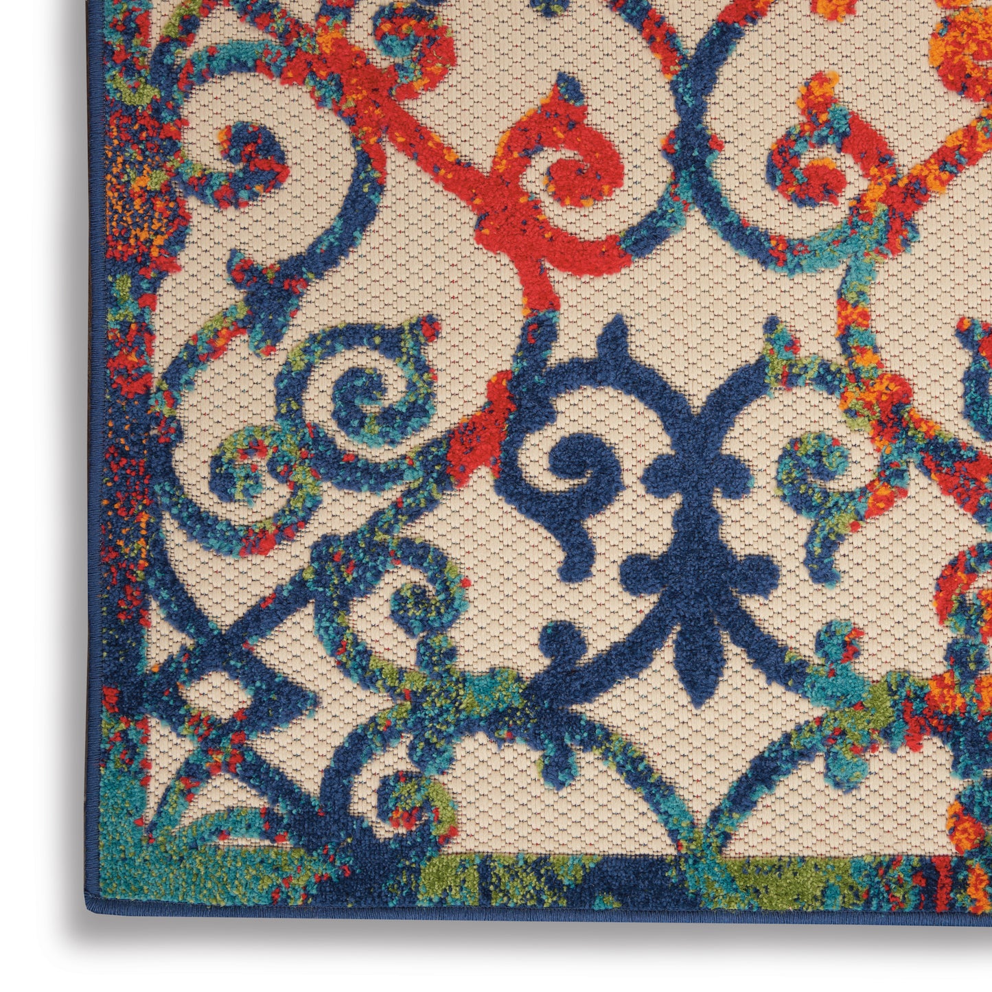 Close-up of a rug with blue scrollwork, dark blue border, floral accents on beige, ornate wrought-iron style pattern.