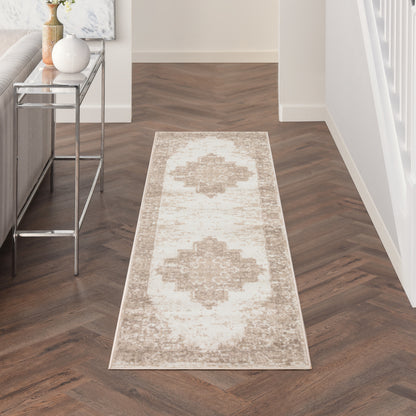 Long beige runner rug with taupe medallion pattern on dark herringbone floor beside a glass-top console in a bright hallway.