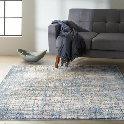Grey fabric sofa with wooden legs, blue throw, ceramic bowl on light wood floor, and a blue patterned area rug.