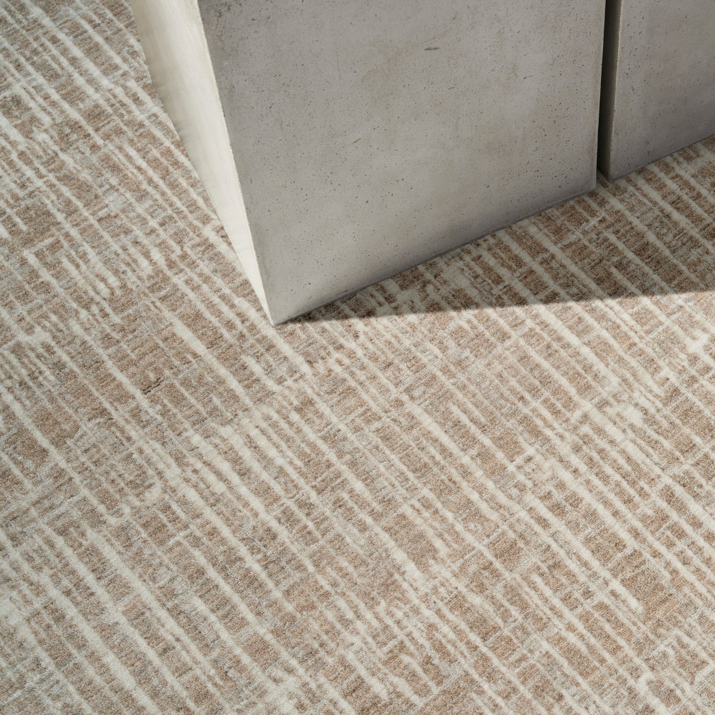 Grey concrete block corner resting on a beige textured rug with white linear pattern, modern industrial style.