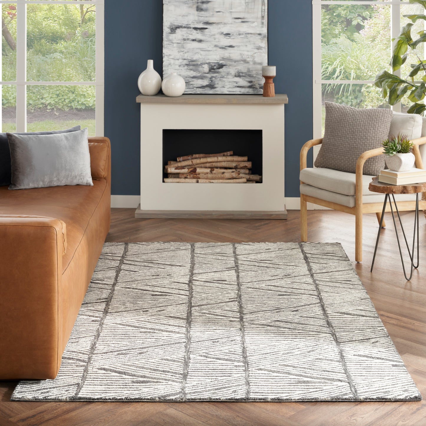 Cozy living room with gray geometric rug (5' x 7'), brown leather sofa, light wood chair, blue wall, white fireplace and stacked logs.