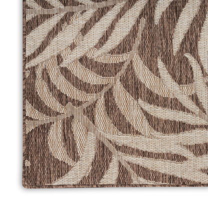 Beige and brown woven rug with large leafy botanical pattern; textured jute-like fabric.