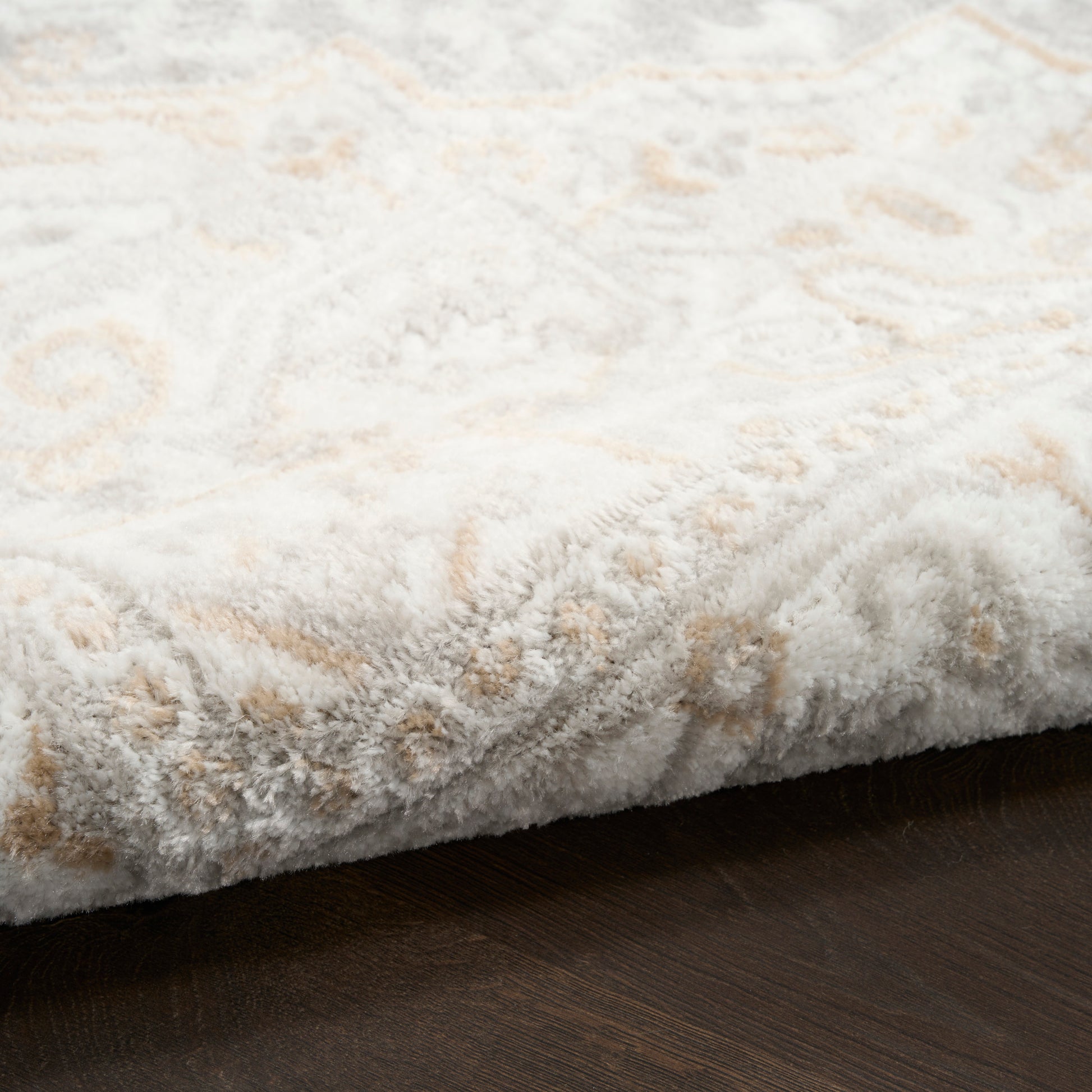 Rectangular plush cream rug with beige geometric pattern, thick pile, edge folded on dark wood floor.