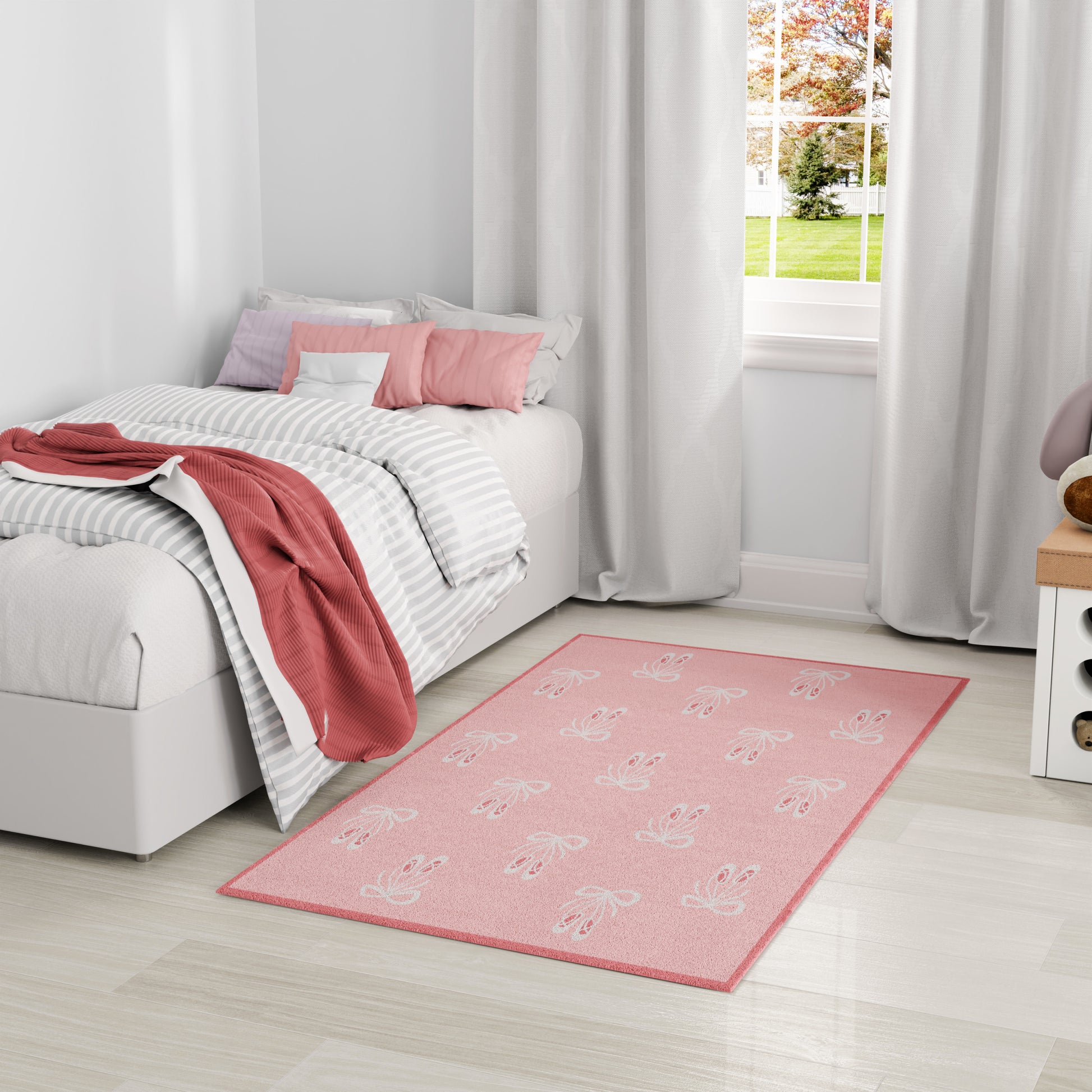 Pink area rug with white leaf patterns in a bright bedroom with striped gray bedding and white curtains.