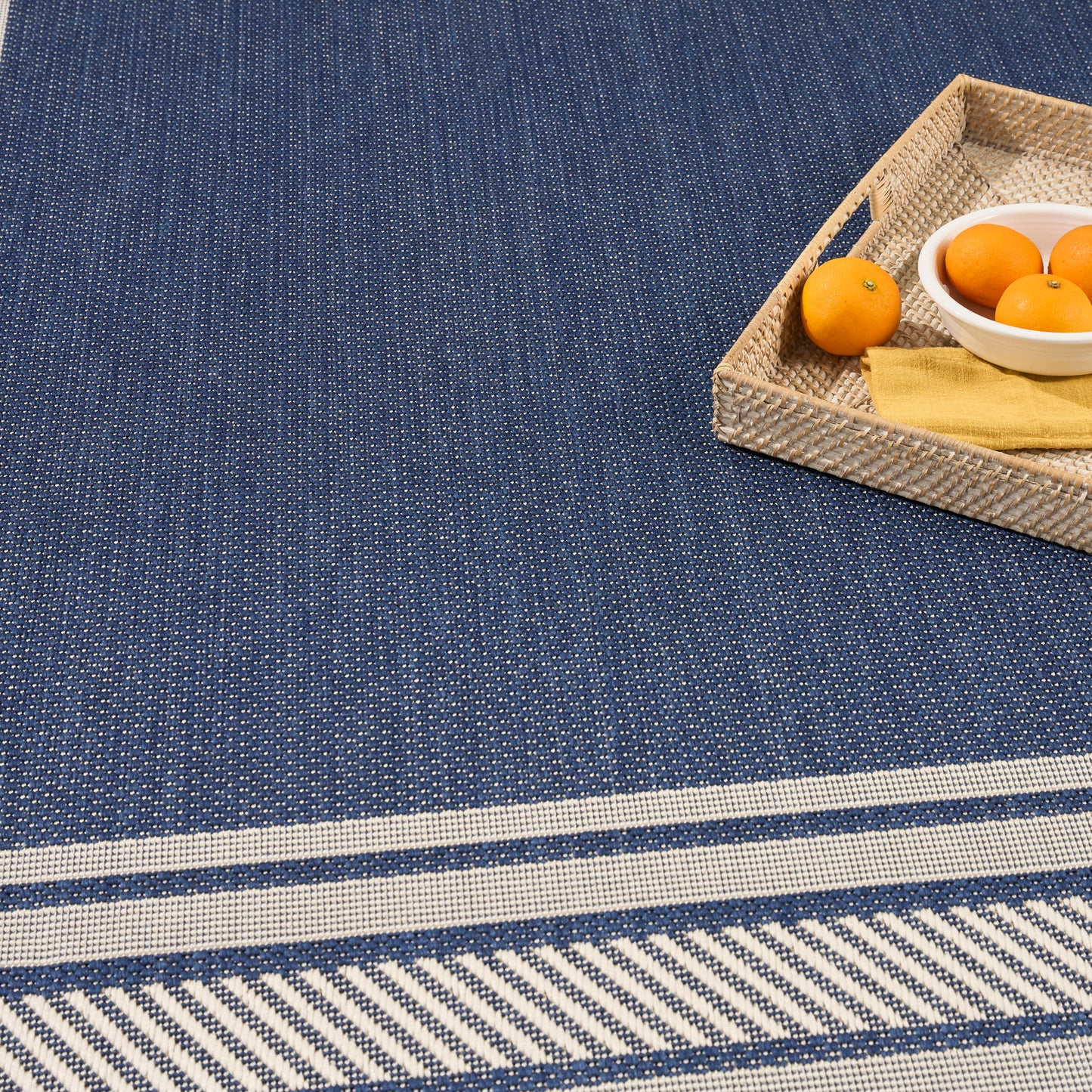 Blue woven rug with white stripes; wicker tray with oranges and a yellow napkin.