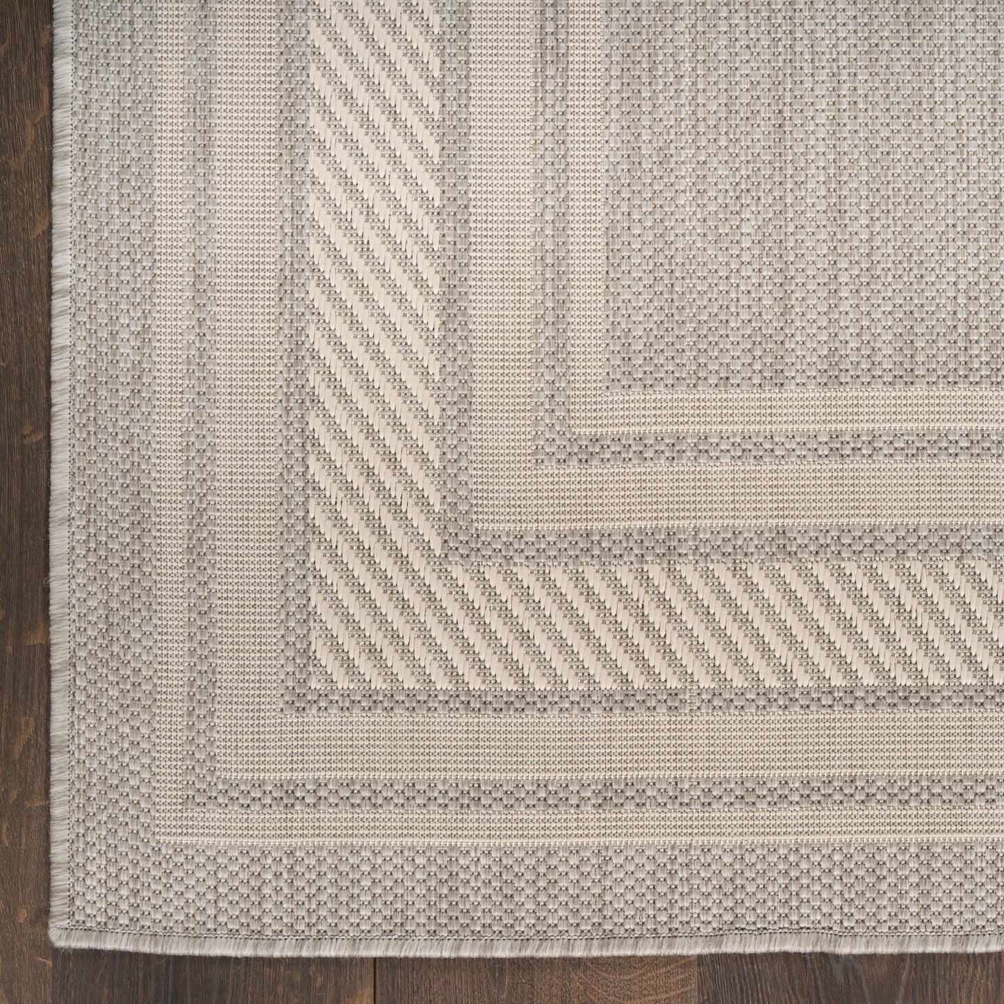 Beige woven runner rug with concentric rectangular borders, diagonal ribbed bands, and a fringed edge on dark wood floor.