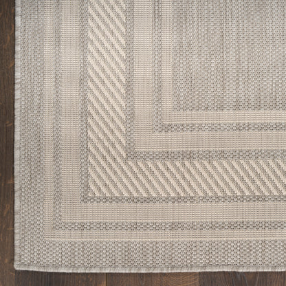 Beige woven runner rug with concentric rectangular borders, diagonal ribbed bands, and a fringed edge on dark wood floor.