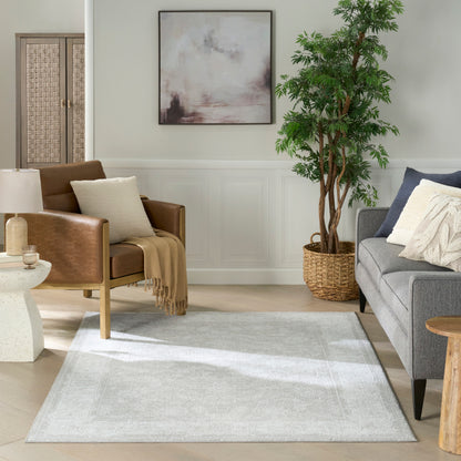 Cozy living room with brown leather armchair, beige throw, gray sofa, tall plant in a woven basket, abstract art, and light gray area rug.