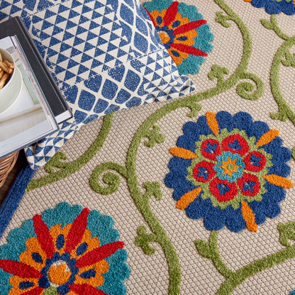 Close-up of a beige floral rug with blue and orange medallion flowers and green vines, beside a blue geometric pillow