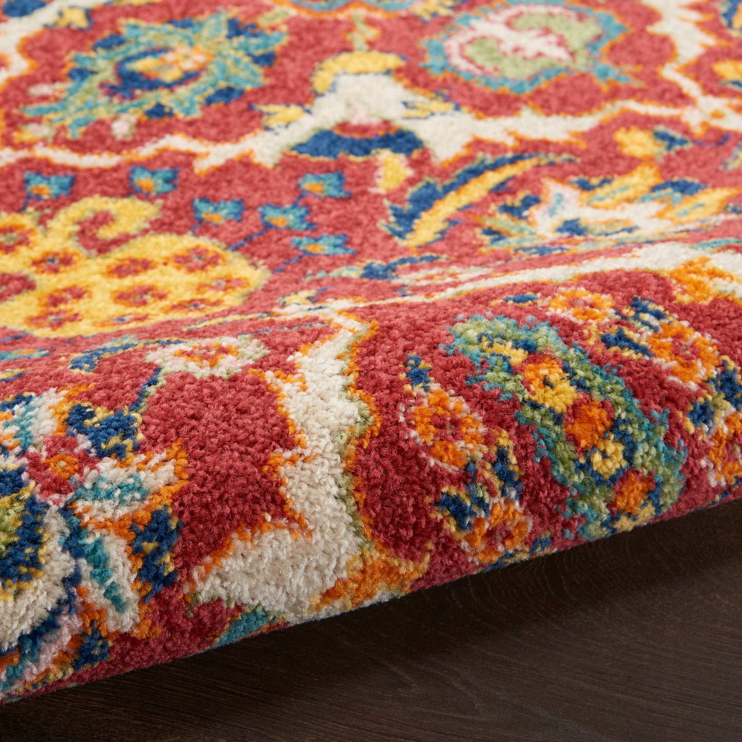 Close-up of a plush Persian-style runner rug with red, yellow, blue and teal floral motifs on dark wood floor.