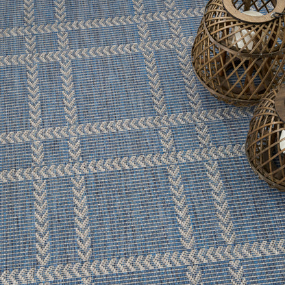 Blue woven rug with cream braided borders forming a grid pattern; wicker lanterns in the top-right corner.