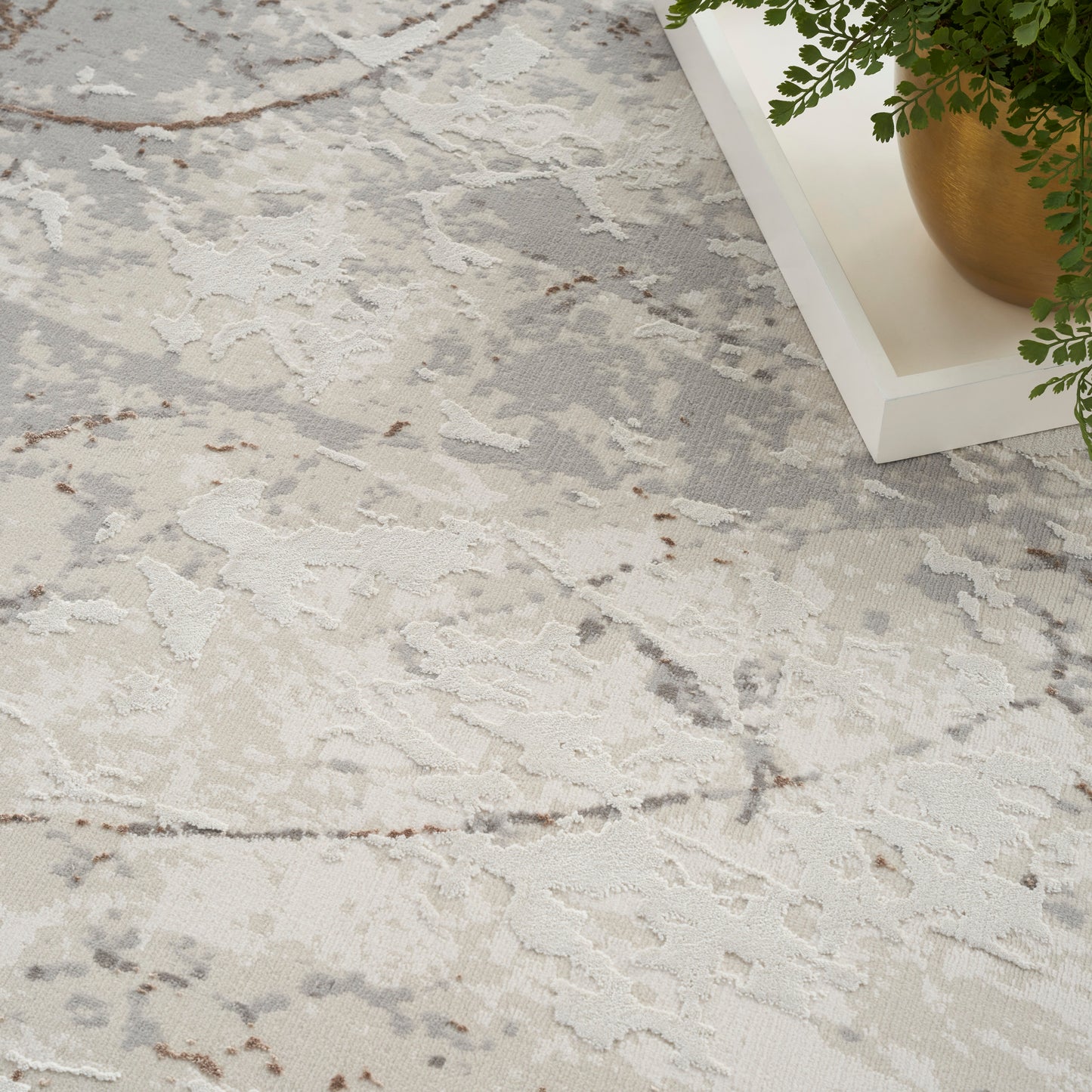 Cream and gray abstract-pattern rug with soft marbling and subtle brown veins, plush texture beside a white tray and green plant.