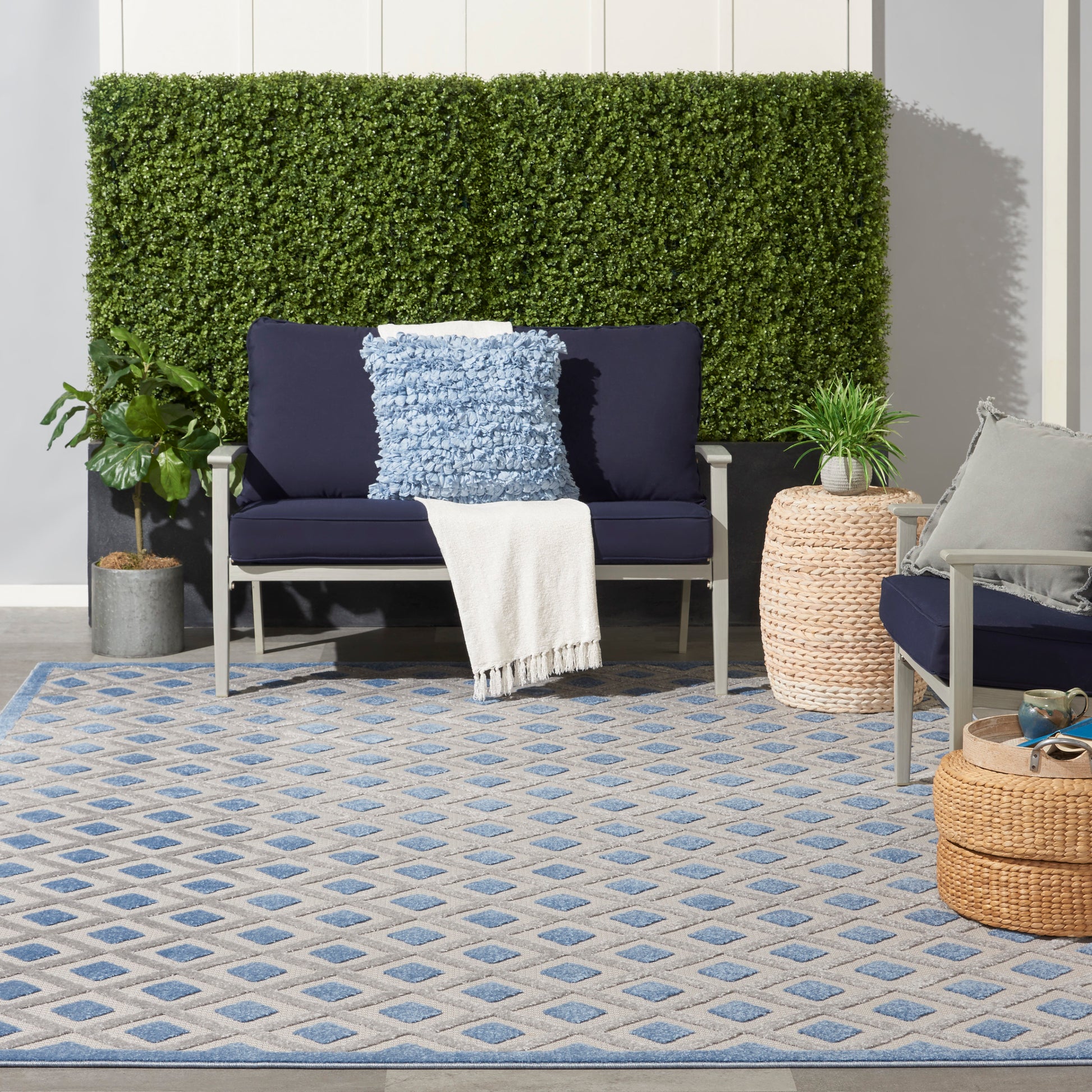 Blue-beige diamond-pattern rug; visible are navy cushions on a gray metal-framed seating area, with a blue textured pillow and a beige throw.