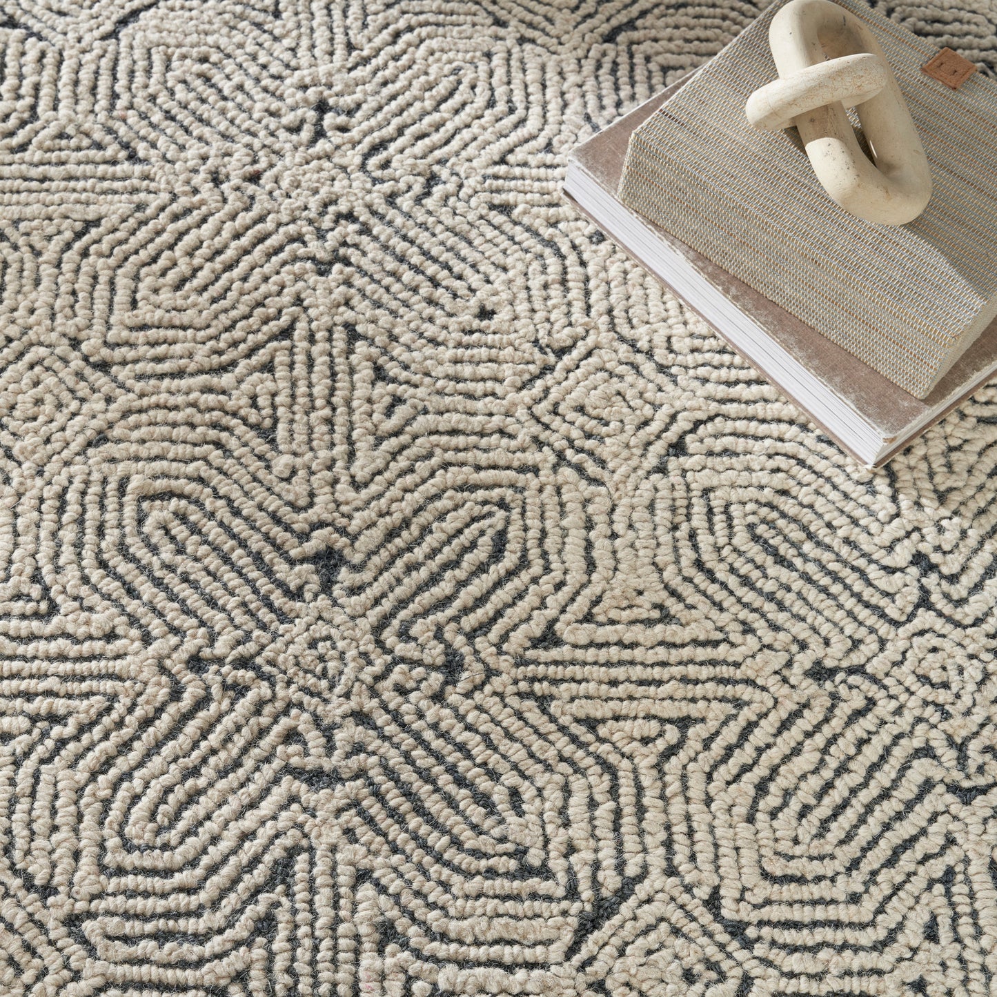 Cream and charcoal geometric shag rug with a raised loop pattern; beige woven tray with ivory handle sits on top.