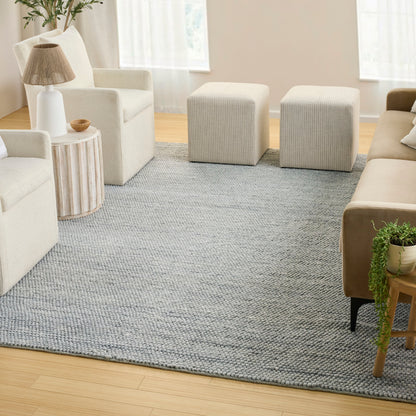 Neutral living room with cream sofas, two gray ottoman poufs, textured gray rug, wooden side table, lamp and greenery.