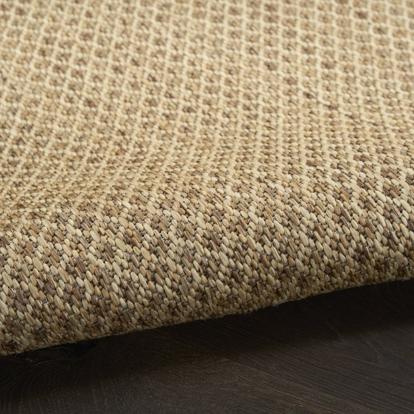 Close-up of a natural jute rug with beige-tan woven texture on dark wood flooring.