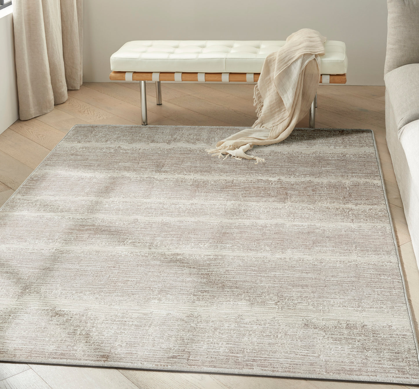Neutral beige and taupe rug with soft gradient on light wood floor, paired with white tufted bench and beige throw.