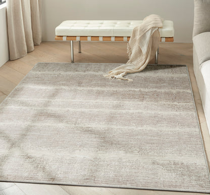 Neutral beige and taupe rug with soft gradient on light wood floor, paired with white tufted bench and beige throw.