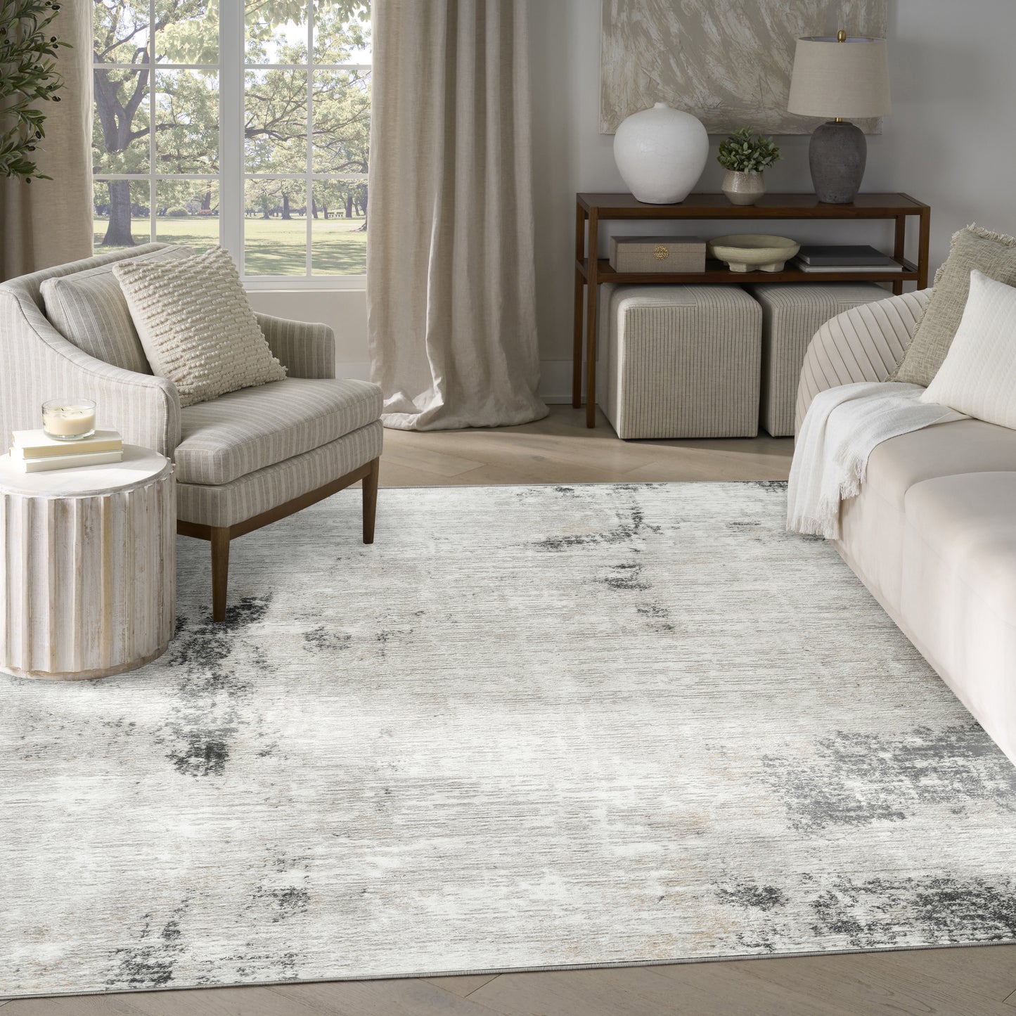 Neutral living room with cream sofa and armchair, textured rug, wooden console, round side table, and beige curtains.