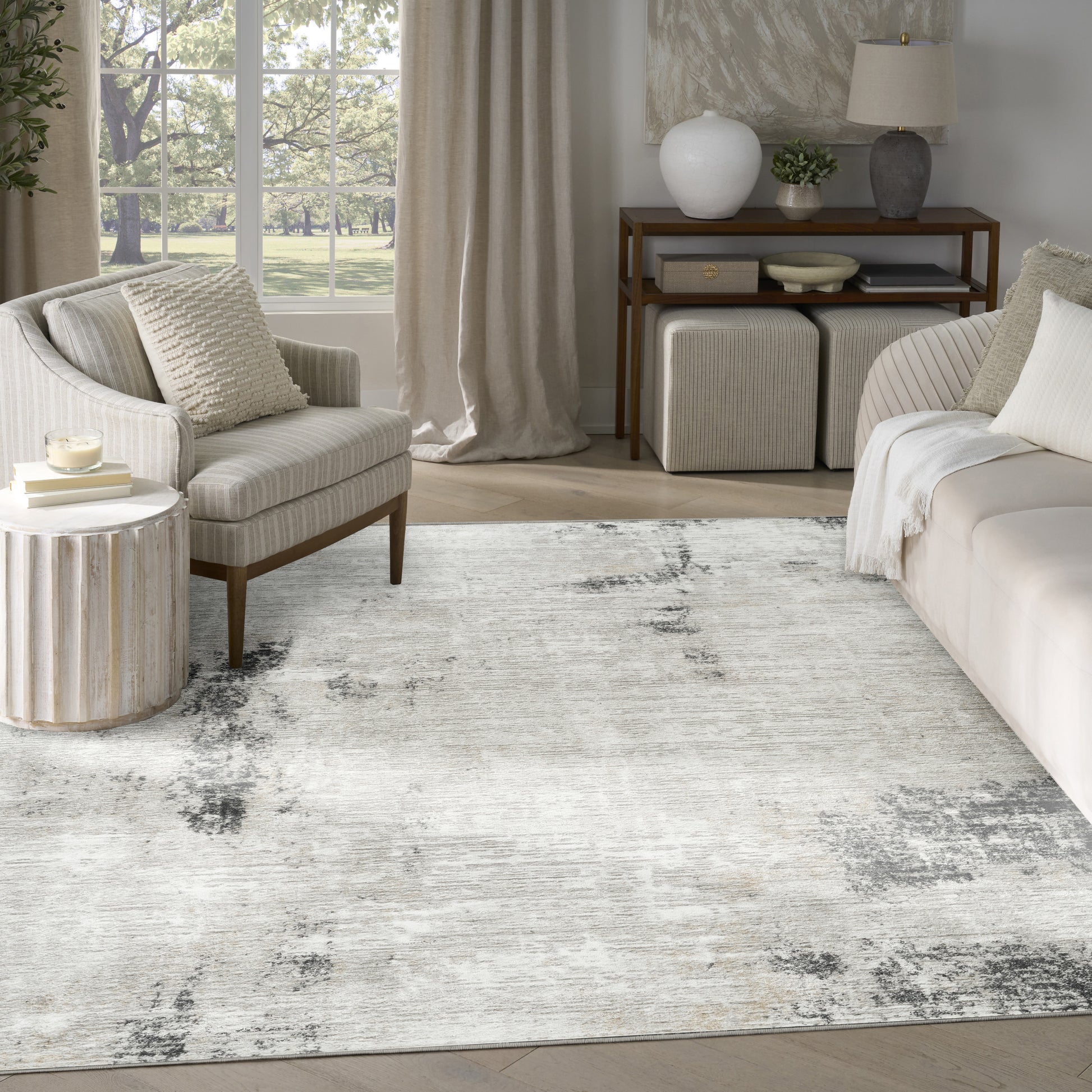 Neutral living room with cream sofa and armchair, textured rug, wooden console, round side table, and beige curtains.