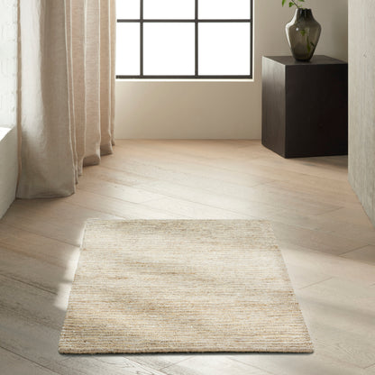 Beige woven rug on light wood floor in bright room with large grid window, cream curtains, and black pedestal vase.