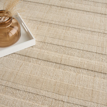 Beige woven rug with amber glass vase and dried grasses on a white tray.