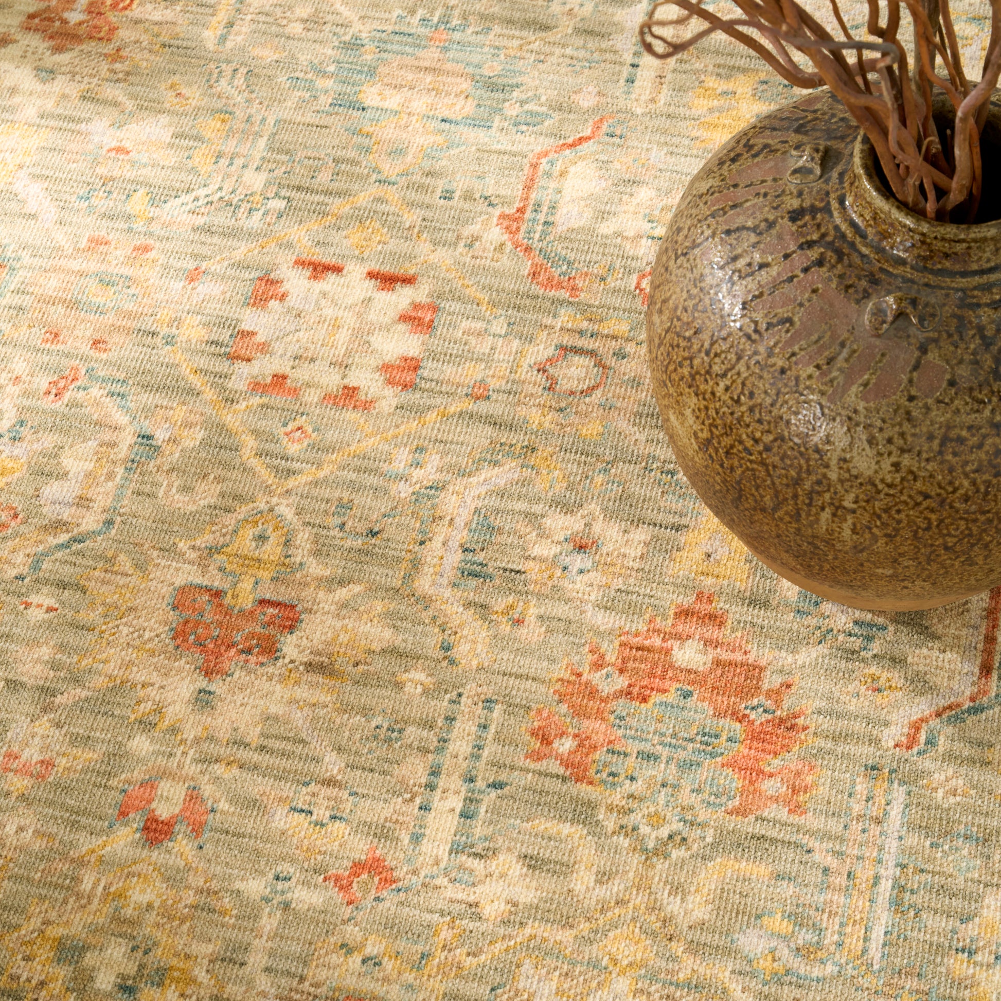 Distressed vintage oriental rug in beige with blue, peach and orange geometric motifs, paired with a rustic ceramic vase.