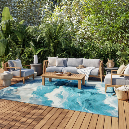 Outdoor sofa set with gray cushions on teak frames, rectangular coffee table, and a blue marble-pattern rug amid tropical plants.