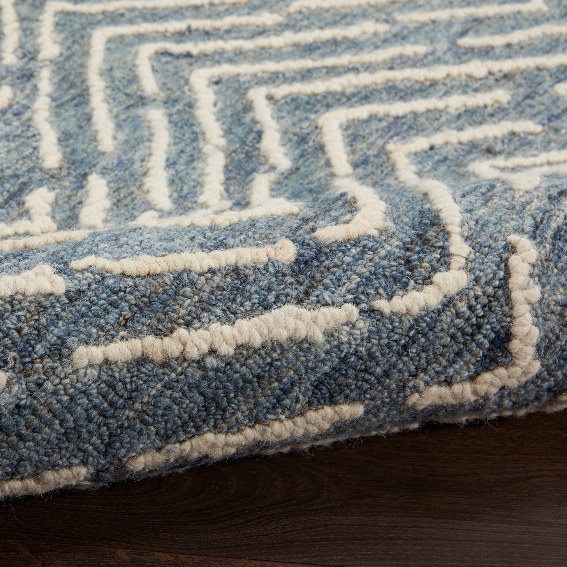 Blue shag rug with white raised maze pattern, plush loop-pile, edge fringe on dark wood floor.