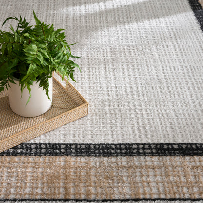 Green fern in a white pot on a woven beige tray atop a cream and tan patterned rug with a black border.