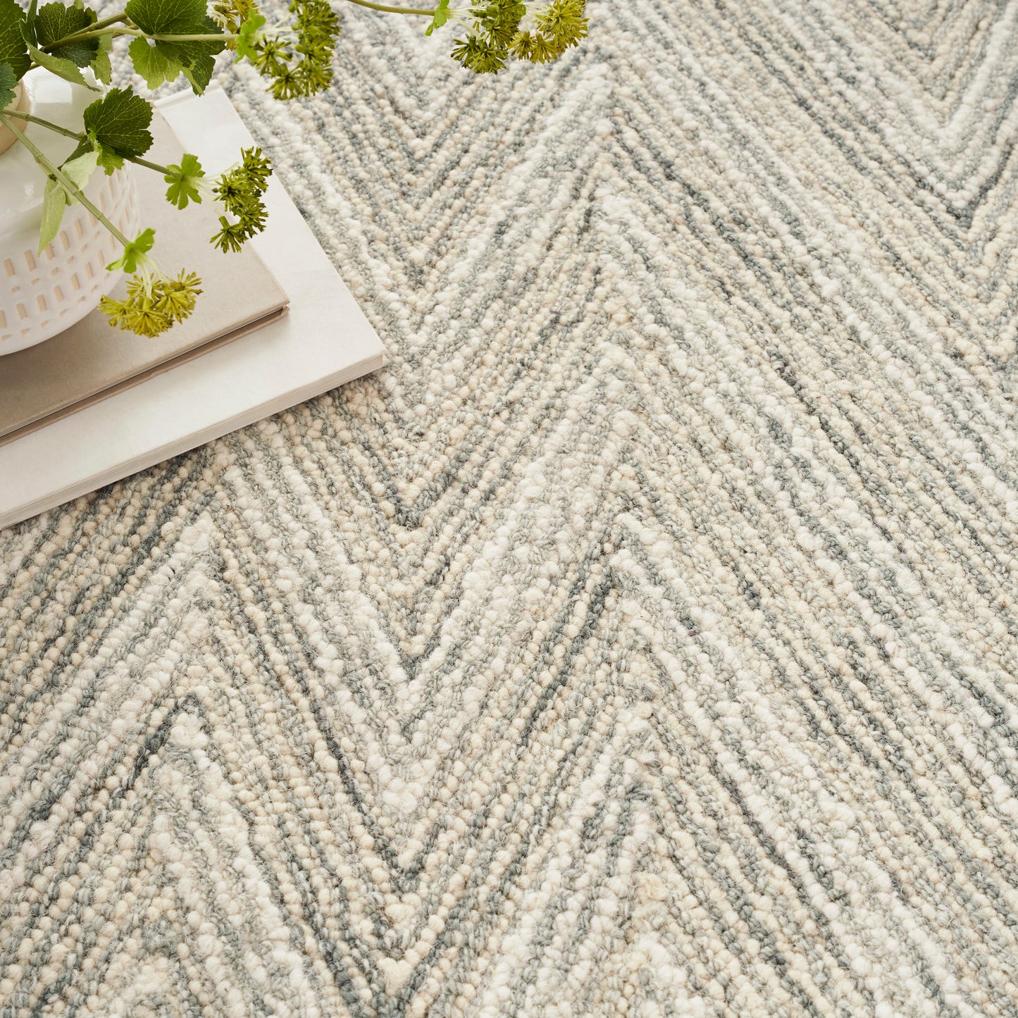 Light gray chevron shag rug in cream tones, with a stack of books & a white planter with green flowers.