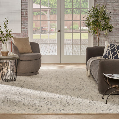 Neutral living room with beige rug, round gray chair, dark sofa, navy geometric pillow, glass French doors, brick walls.