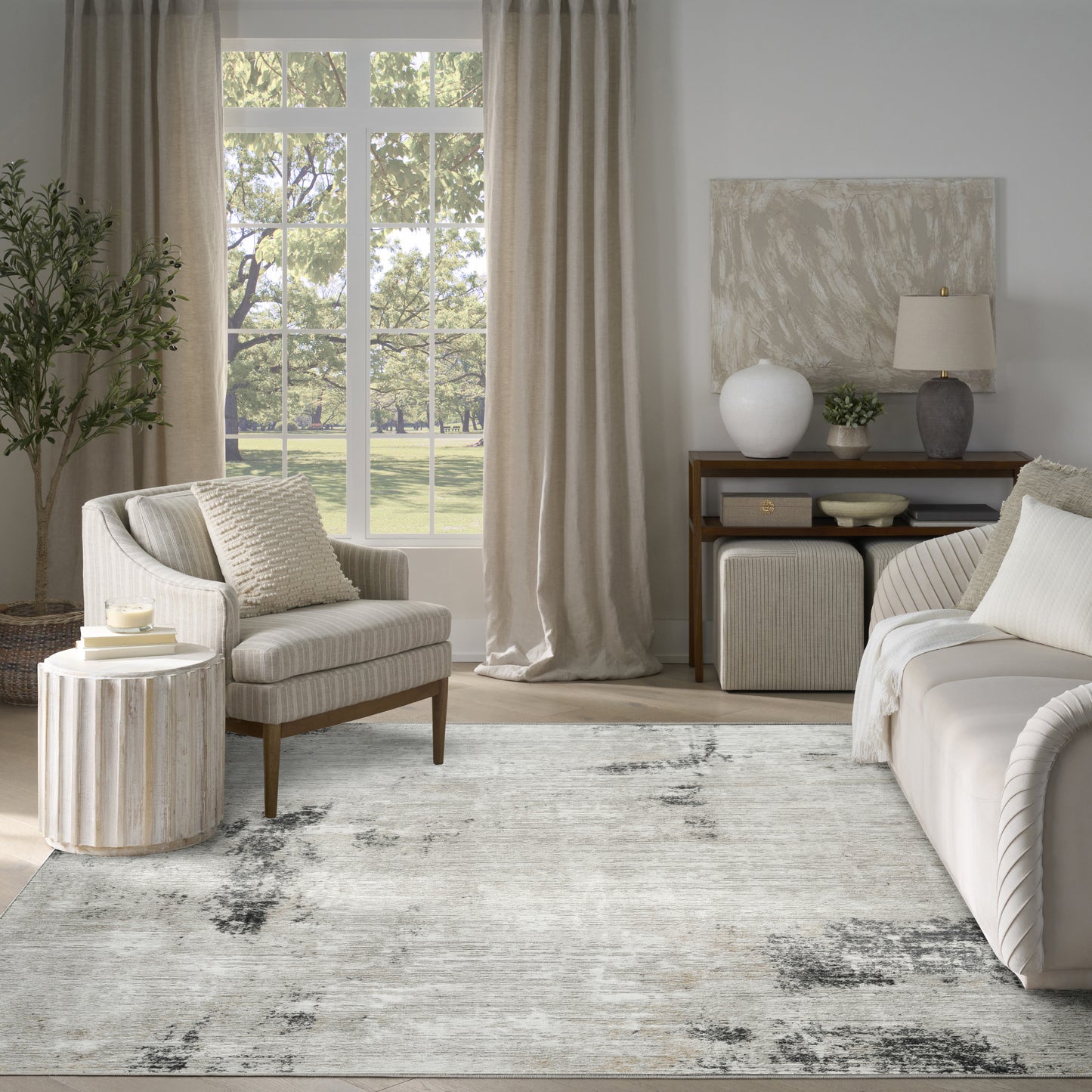 Neutral living room with beige sofa, striped armchair, round ribbed wood side table, soft cushions, light rug, curtains.